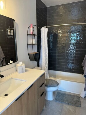 A modern bathroom with a bathtub, toilet, and a vanity with a mirror and storage shelves.