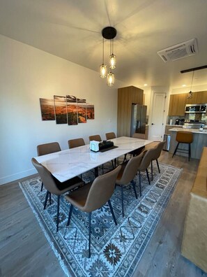 A modern dining area with a long table, multiple chairs, and a patterned rug.