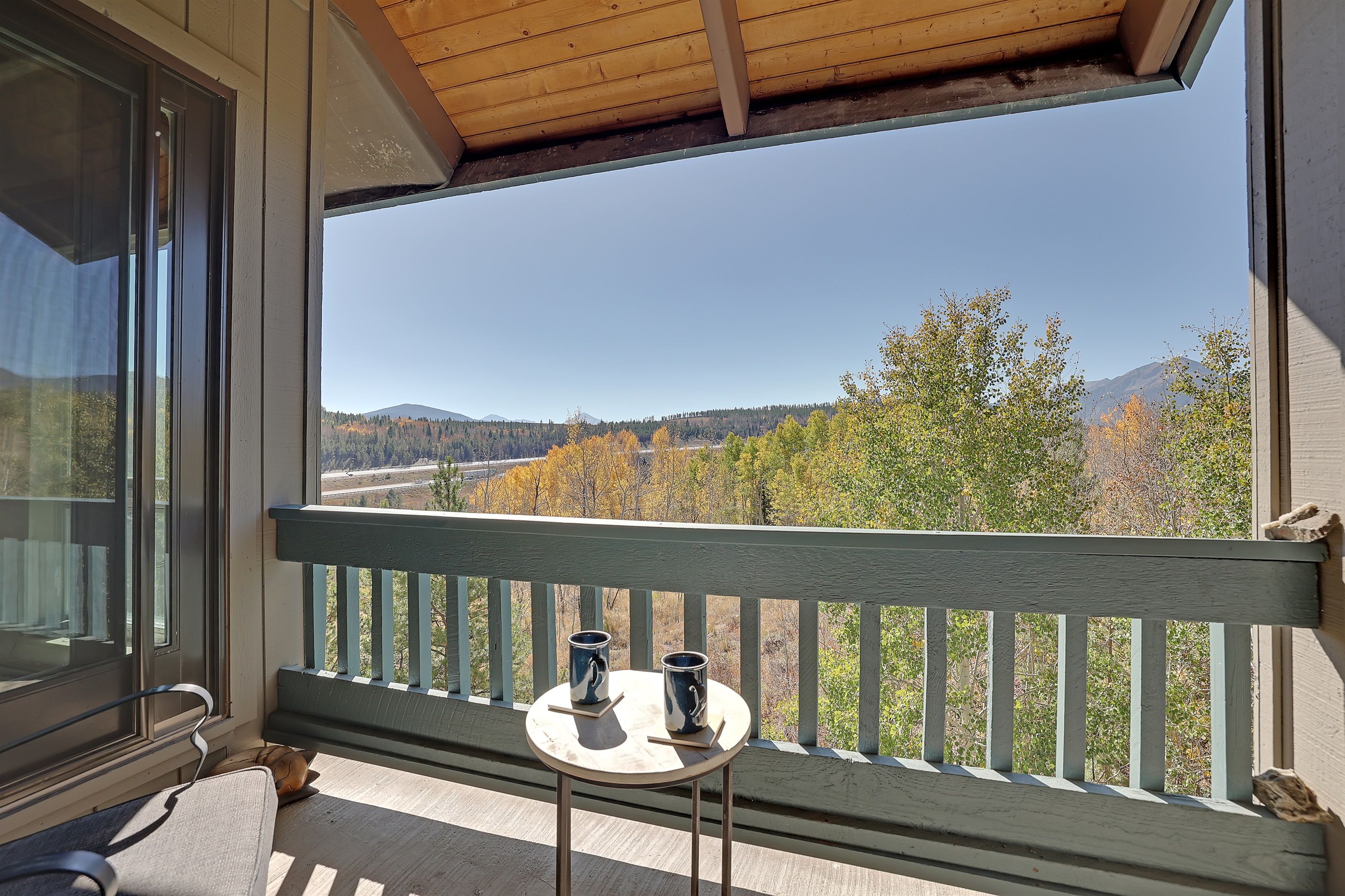 En balkon med et bord og to kopper, med udsigt over et naturskønt landskab med træer og bjerge.