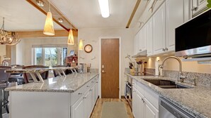 A modern kitchen with granite countertops, white cabinetry, a built-in dishwasher, and pendant lighting.