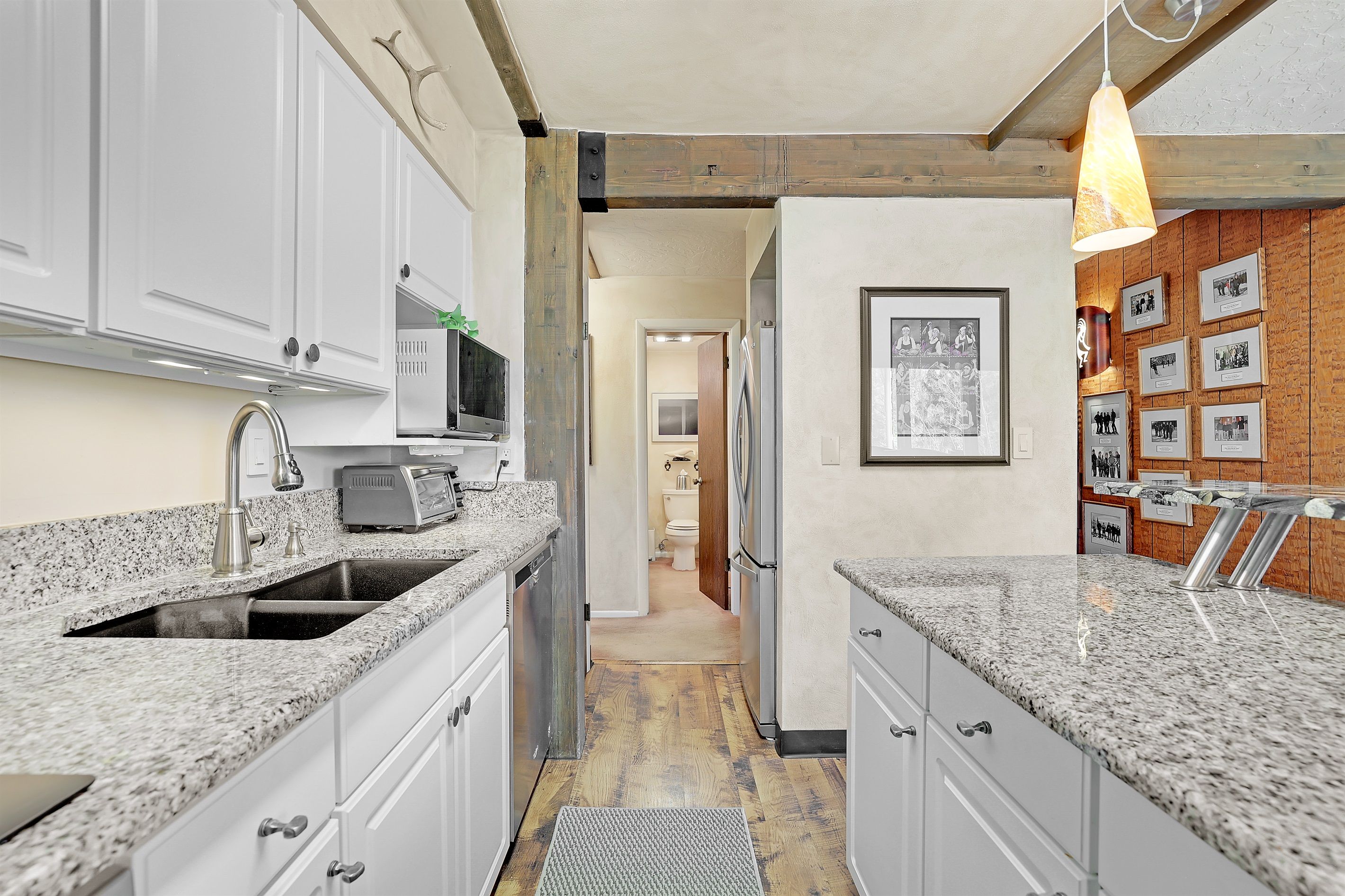 A modern kitchen with granite countertops, white cabinets, a microwave, and a hanging pendant light.