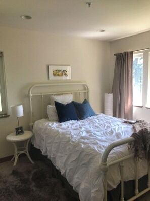 A bed with white bedding, a headboard, and a bedside table with a lamp. - Charming 3-bedroom house in Vashon with cool AC breeze (Vashon)