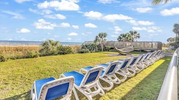 A row of blue lounge chairs on a grassy area with a wooden boardwalk and palm trees in the background.