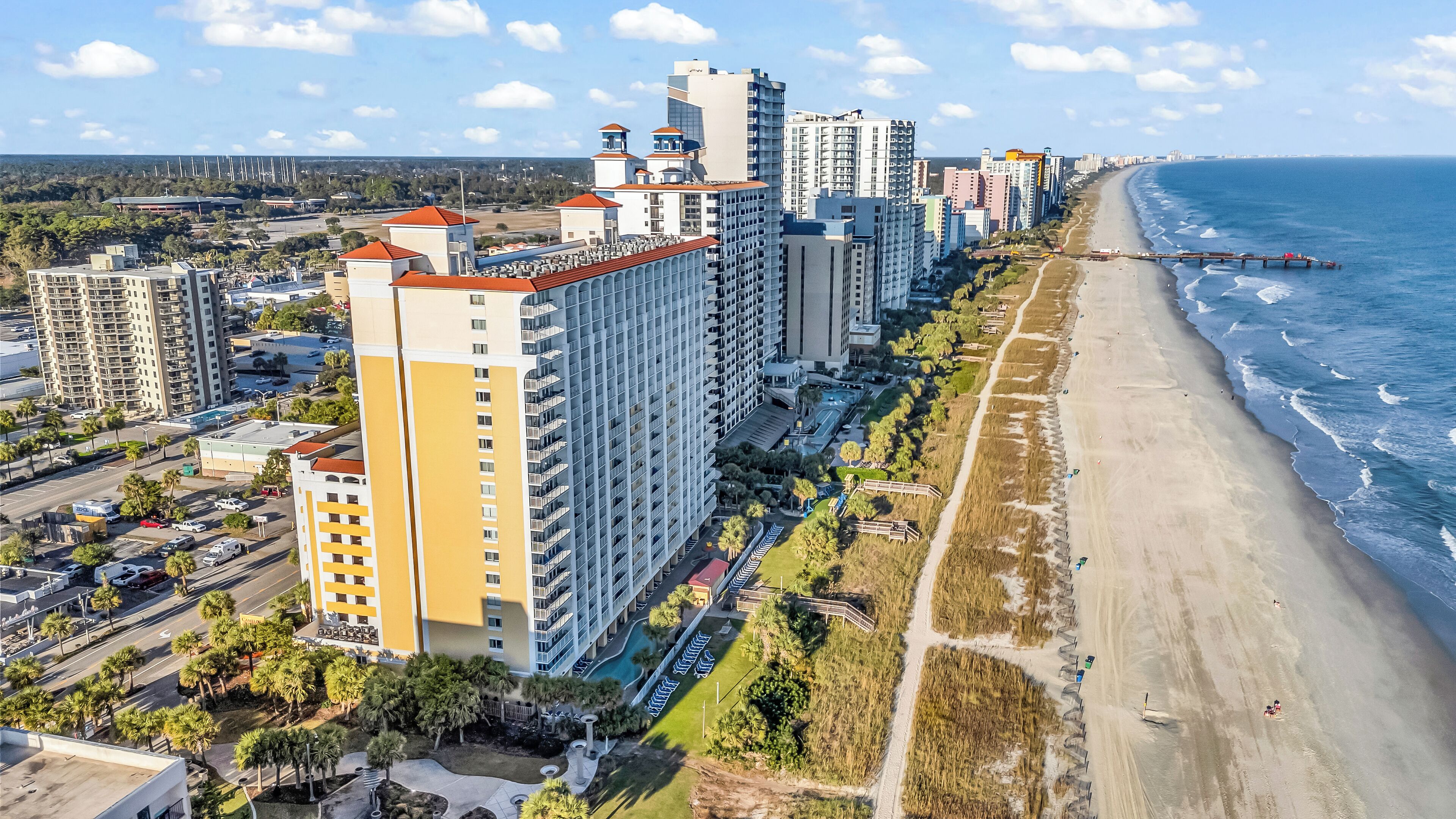 A coastal cityscape with high-rise buildings, a beach, and a pier.