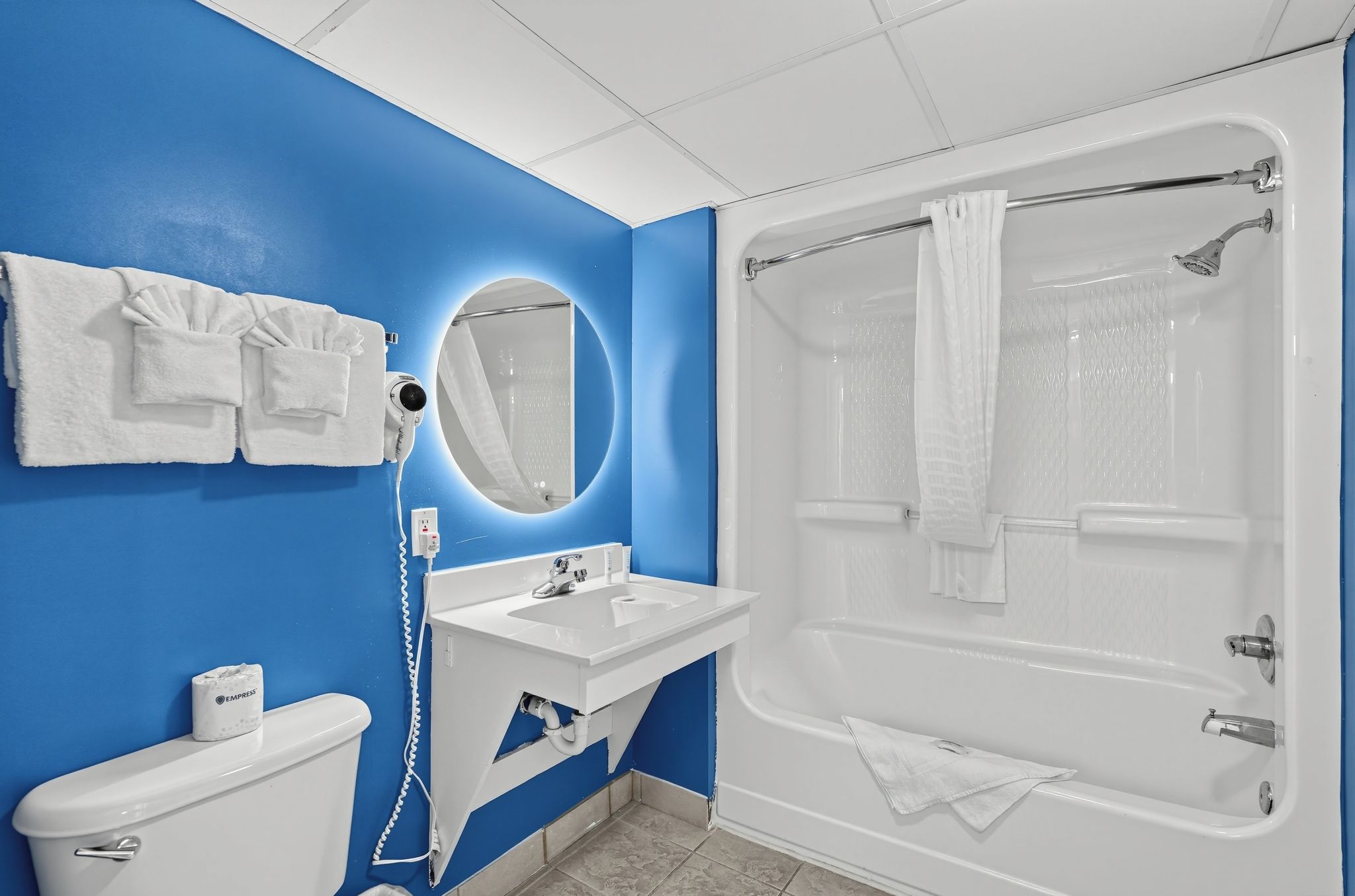 A bathroom with a blue wall, white fixtures, a bathtub, and a mirror.