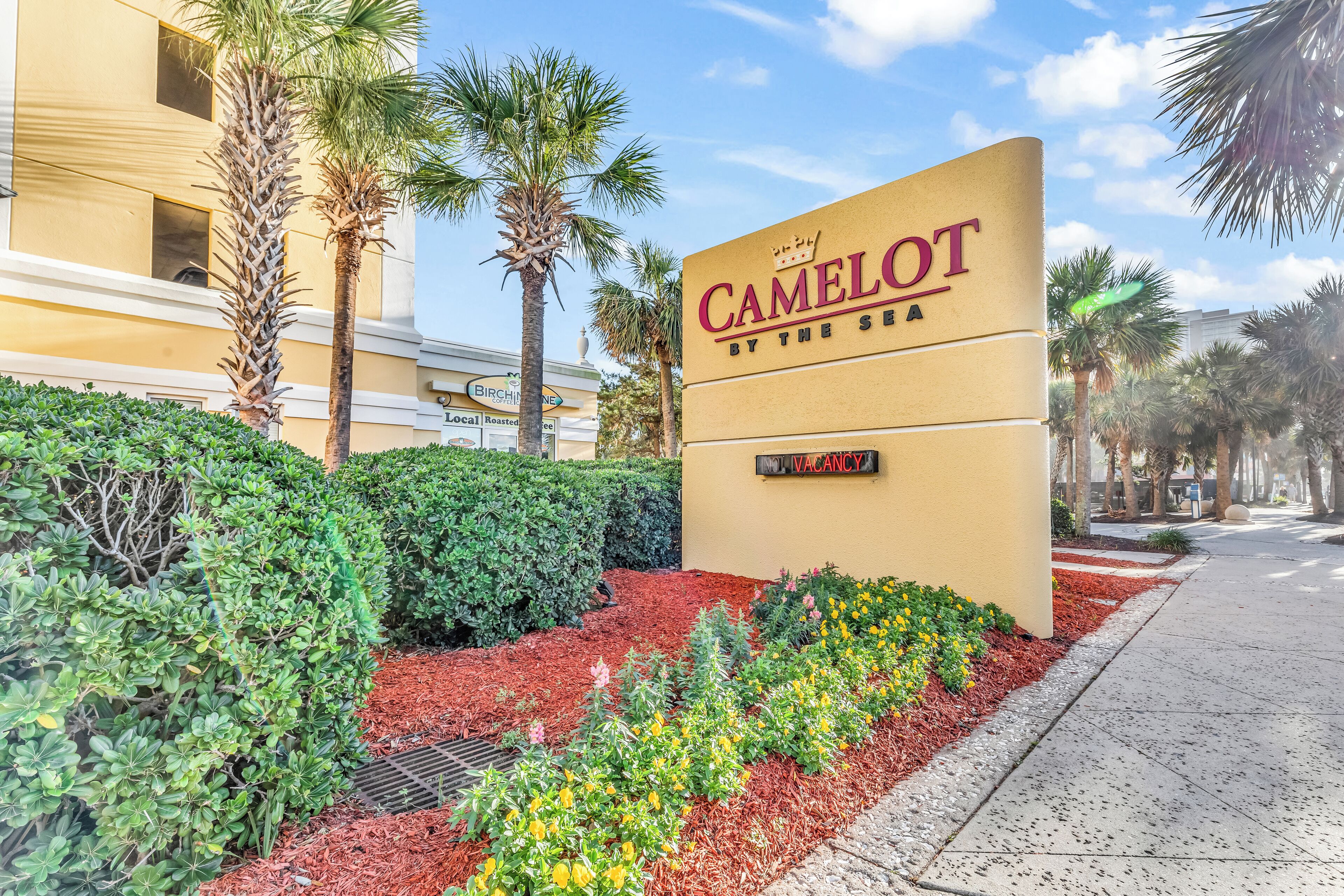 Un letrero de hotel con la inscripción "CAMELOT BY THE SEA" y un anuncio que dice "VACANCIA" debajo.