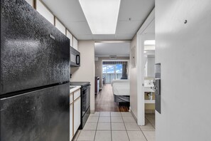 Ein schmaler Flur mit einer Küchenzeile auf einer Seite, einem Bett auf der anderen und einem Fenster mit Blick zum Himmel.