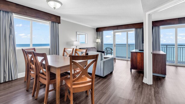 A spacious living area with a dining table, chairs, a sofa, and a view of the ocean. - Camelot By the Sea (Myrtle Beach)