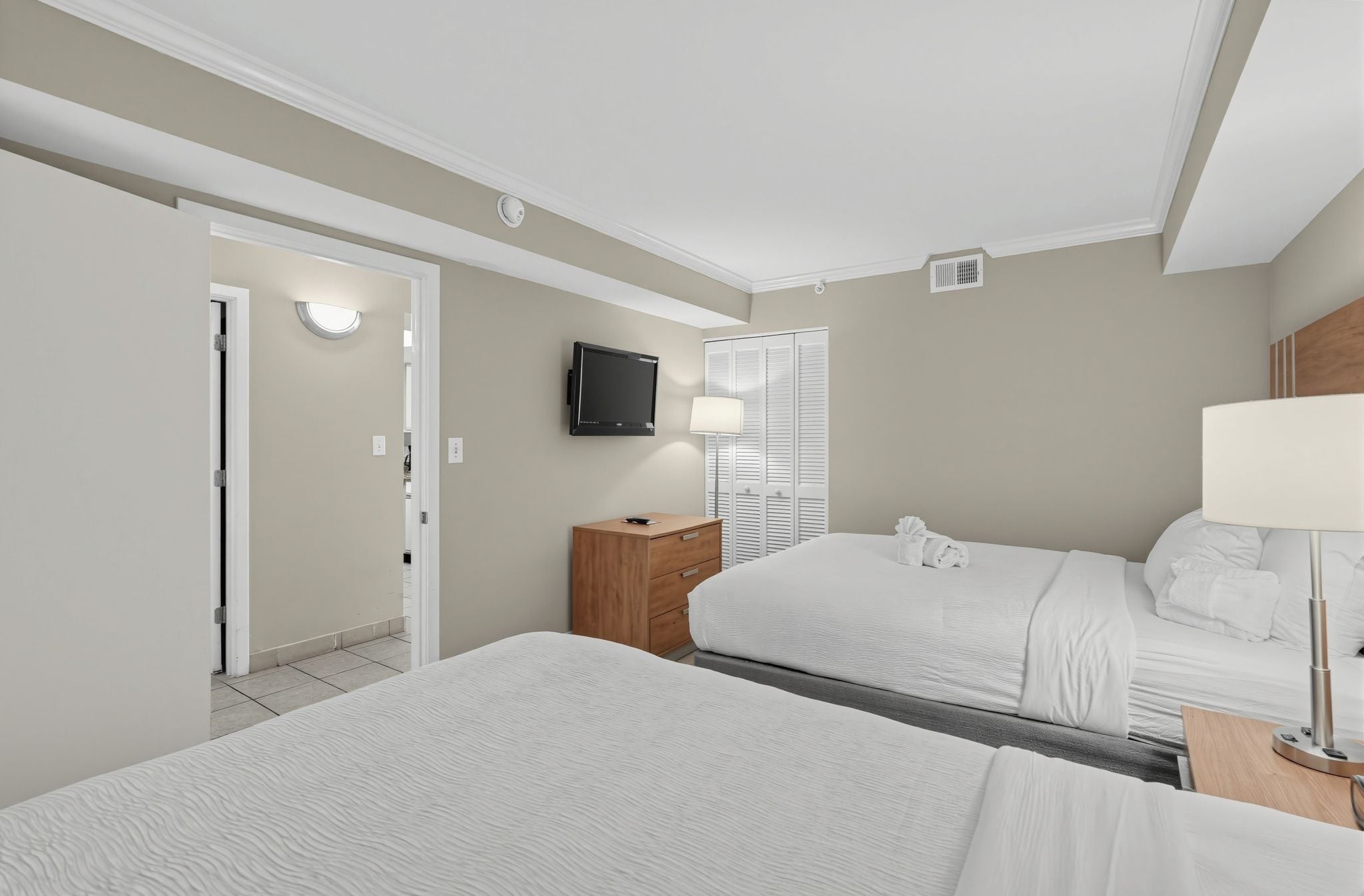 A hotel room with two beds, a television, a bedside lamp, and a wardrobe.