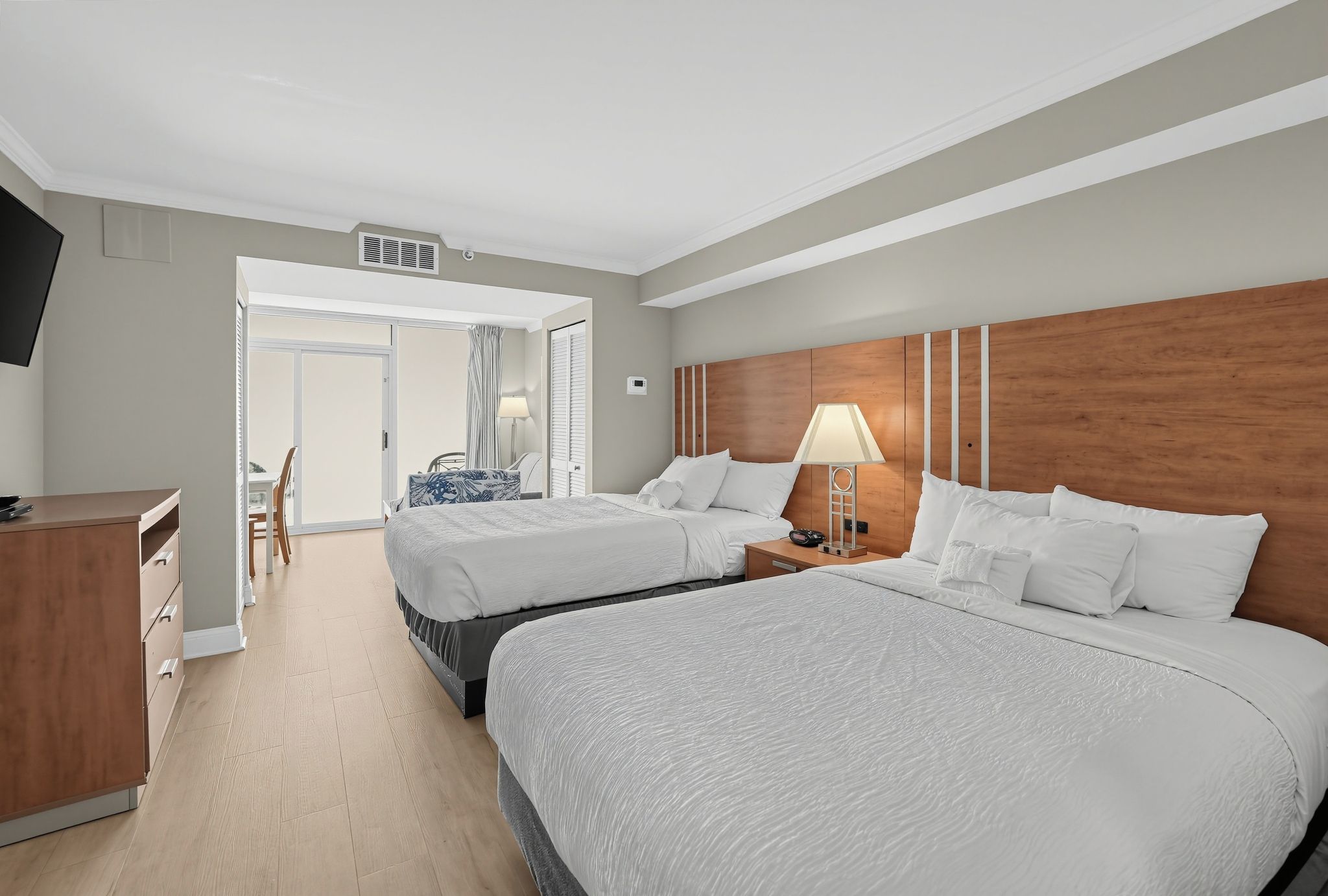 A hotel room with two beds, a desk, a chair, a lamp, and a view of the outside.