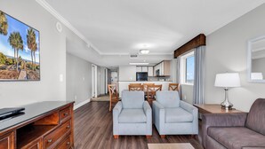 A spacious living area with a flat-screen TV, a wooden desk, two armchairs, a sofa, and a dining table with chairs. - Camelot By the Sea (Myrtle Beach)