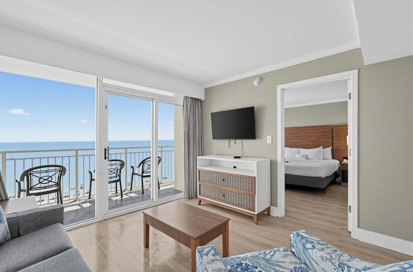 Habitación de hotel con balcón, televisión, cama y zona de estar.
