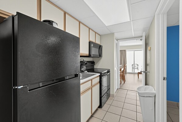 Una cocina moderna con un refrigerador negro, un microondas y una estufa. Se ve un comedor con una mesa y sillas a través de un umbral abierto.
