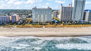 A beachfront hotel with multiple high-rise buildings, a sandy beach, and waves crashing onto the shore. - Camelot By the Sea (Myrtle Beach)