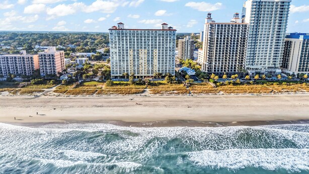 Ein Strandhotel mit mehreren Hochhäusern, einem Sandstrand und brechenden Wellen.