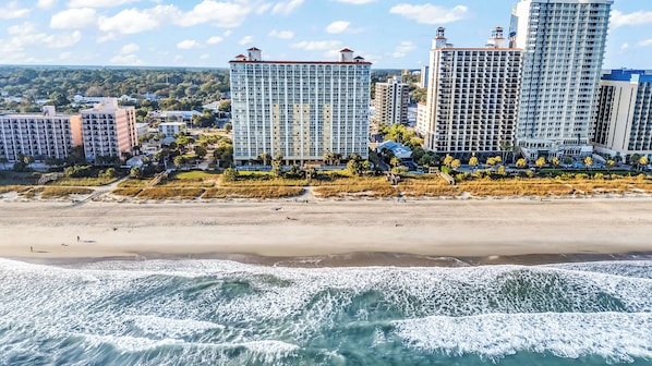 Ein Strandhotel mit mehreren Hochhäusern, einem Sandstrand und brechenden Wellen.