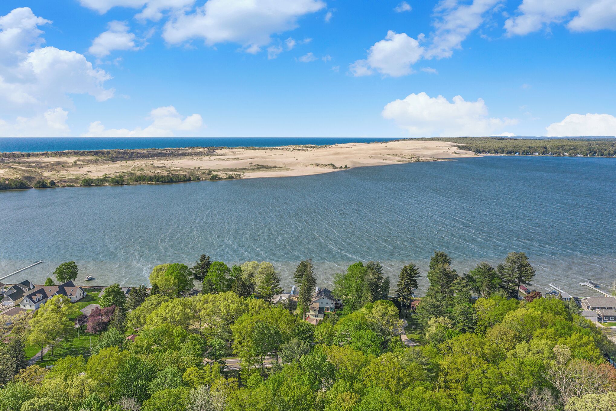 A coastal view with a sandy beach, a marina, and a residential area with houses and trees.
