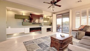 A modern living room with a fireplace, a ceiling fan, and a large window with blinds. - Anthem Getaway with Backyard Oasis!  (New River)