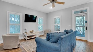 A spacious living room with a large blue couch, a white TV, and a ceiling fan. - The Grey Gull (Panama City Beach)