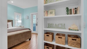 A bedroom with a bed, a bookshelf, and a door leading to another room. - The Grey Gull (Panama City Beach)