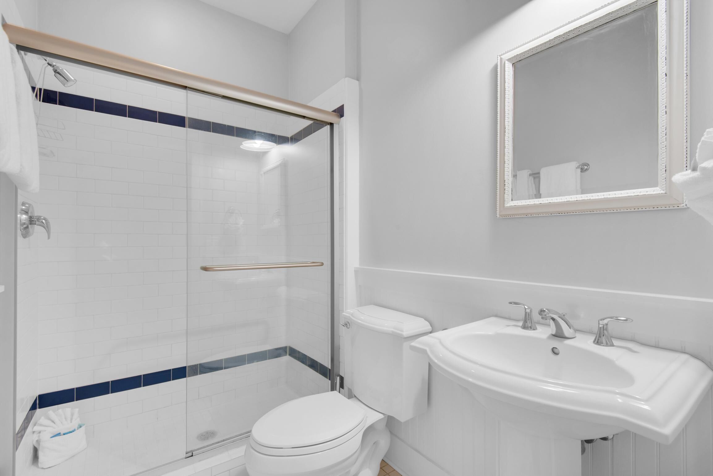 A modern bathroom with a glass shower enclosure, a white toilet, a sink with two faucets, and a mirror above the sink.