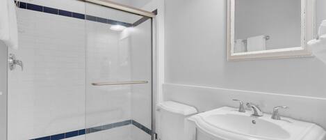 A modern bathroom with a glass shower enclosure, a white toilet, a sink with two faucets, and a mirror above the sink.