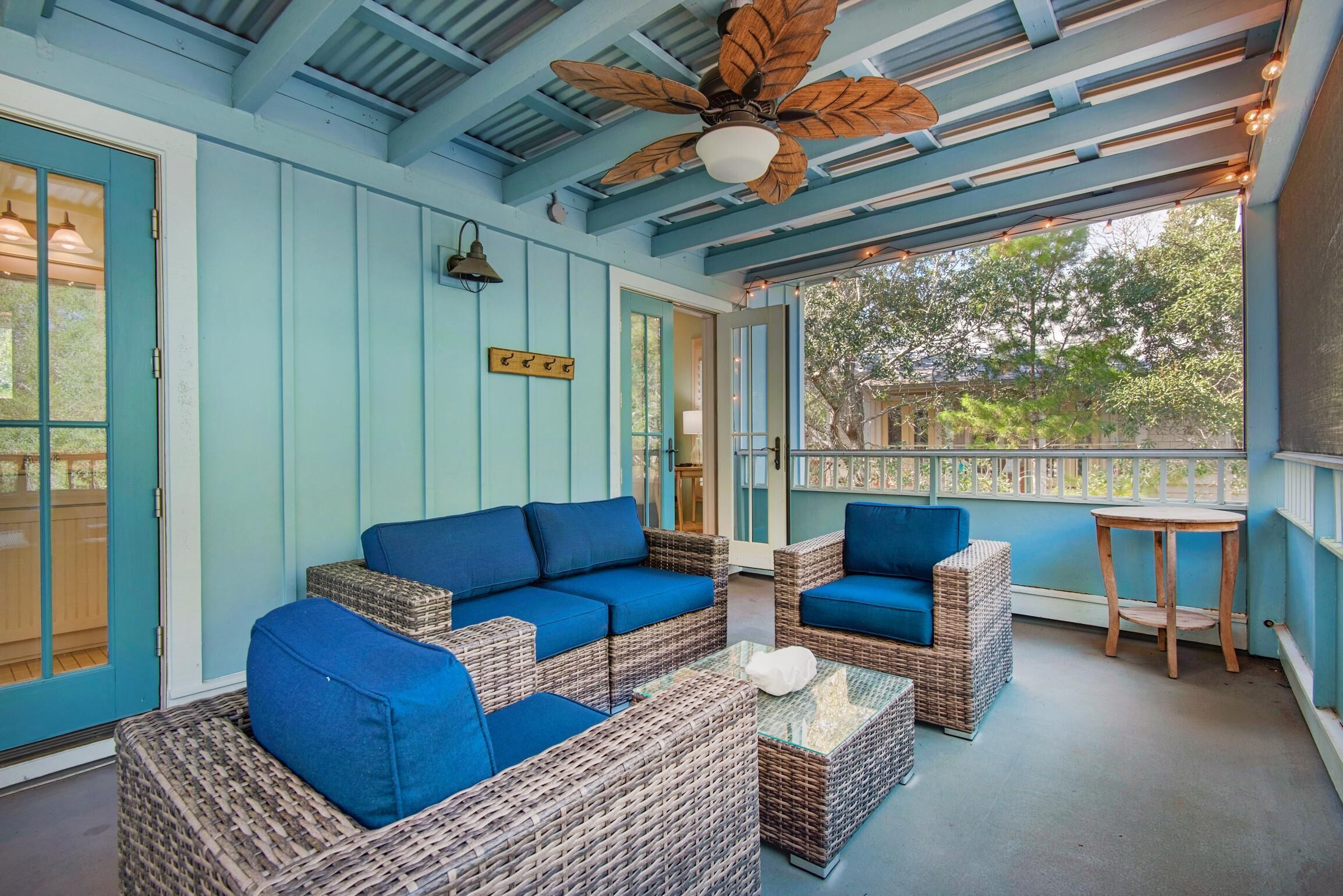 A covered porch with wicker furniture and blue cushions, a ceiling fan, and a view of the outdoors.