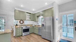 A modern kitchen with green cabinets, stainless steel appliances, and a wooden floor. - The Grey Gull (Panama City Beach)