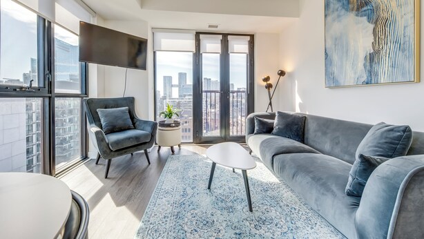 A modern living room with a grey sofa, a black armchair, and a white coffee table. - King W/Queen W : 3br w rooftop BBQ & 360 views (Toronto)