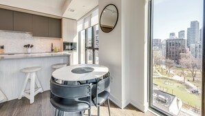 A modern kitchen with a large window, a round dining table with chairs, and a view of a cityscape. - King W/Queen W : 3br w rooftop BBQ & 360 views (Toronto)
