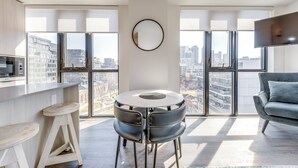 A modern living room with a round table, two chairs, a sofa, and large windows offering city views. - King W/Queen W : 3br w rooftop BBQ & 360 views (Toronto)