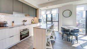 A modern kitchen with a central island, built-in appliances, and a city view through large windows. - King W/Queen W : 3br w rooftop BBQ & 360 views (Toronto)