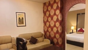 Une chambre d’hôtel avec un canapé, une table en bois, un lit avec un oreiller rouge et un mur à motifs.