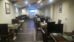 Une salle à manger d’hôtel avec plusieurs tables et chaises, un téléviseur à écran plat fixé au mur et des tableaux encadrés qui décorent les murs.