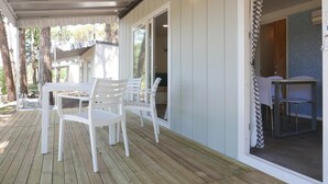 A covered outdoor area with a wooden deck, white plastic chairs, and a table. - Belvedere Pineta Village Adria Home for 6 persons (Belvedere Grado)