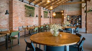 A restaurant with brick walls, hanging light bulbs, and a variety of seating arrangements including round tables and benches.
