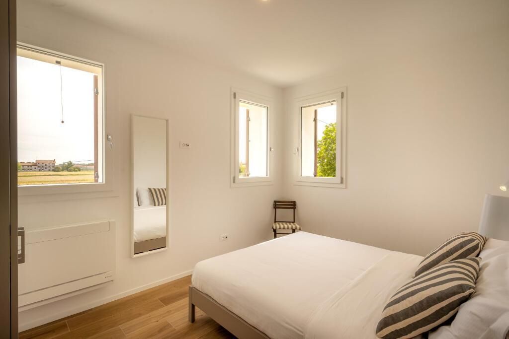 A bedroom with a bed, a radiator, a mirror, and two windows.