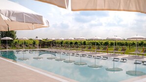 Una piscina con sillones de descanso y sombrillas, rodeada de vegetación.