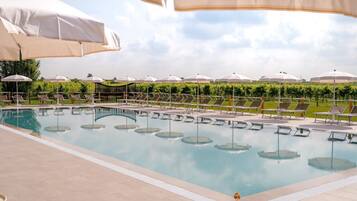 A swimming pool with lounge chairs and umbrellas, surrounded by greenery.
