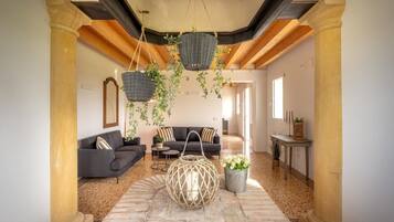 A spacious living area with a stone floor, a dark-colored sofa set, a round woven coffee table, and hanging baskets with greenery.