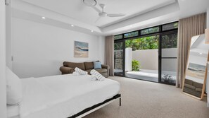 Een moderne slaapkamer met een groot bed, een slaapbank en een balkon met uitzicht op groen.