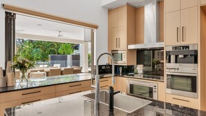 A modern kitchen with a large island, stainless steel appliances, and a view of a patio area. - Villa 8 The Lakes moments from pristine beaches, world-class golf courses, and the stunning Mt. Cool (Mount Coolum)