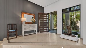 A modern interior with a grey wall, a wooden bench, a white console table with a mirror, and a statue. - Villa 8 The Lakes moments from pristine beaches, world-class golf courses, and the stunning Mt. Cool (Mount Coolum)