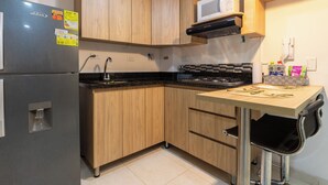 A compact kitchen with wooden cabinets, a built-in microwave, a gas stove, and a refrigerator.