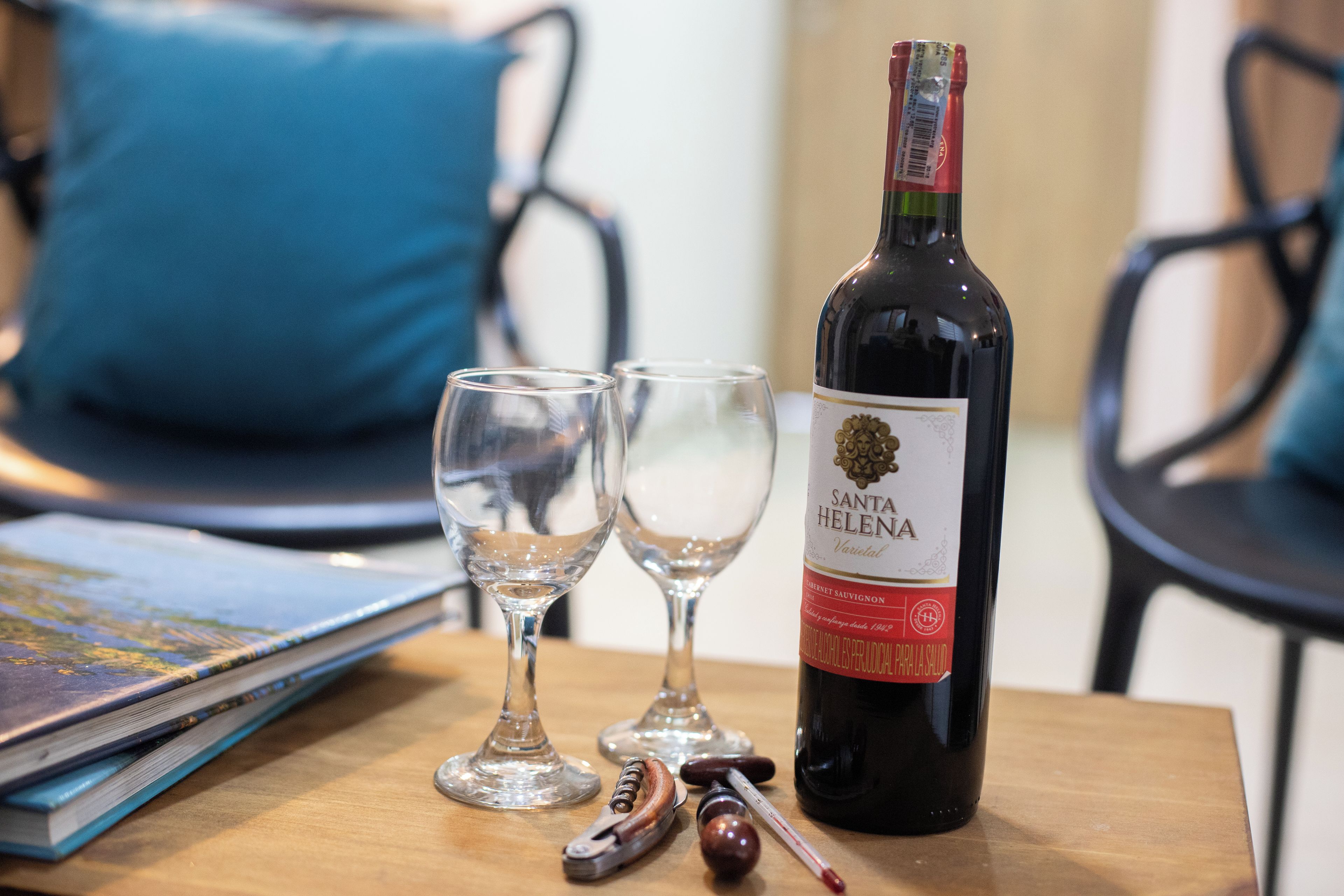 Una botella de vino Santa Helena, dos copas vacías, un sacacorchos y un termómetro sobre una mesa de madera.