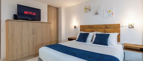A hotel room with a bed, a wooden wardrobe, a television displaying 'NETFLIX', and wall-mounted artwork.