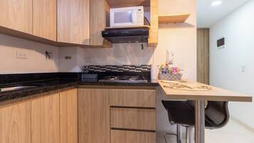 Cocina compacta con armarios de madera, microondas, cocina a gas y un pequeño comedor con una silla.