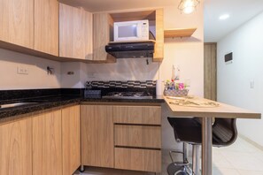 A compact kitchen with wooden cabinets, a microwave, a gas stove, and a small dining area with a chair.