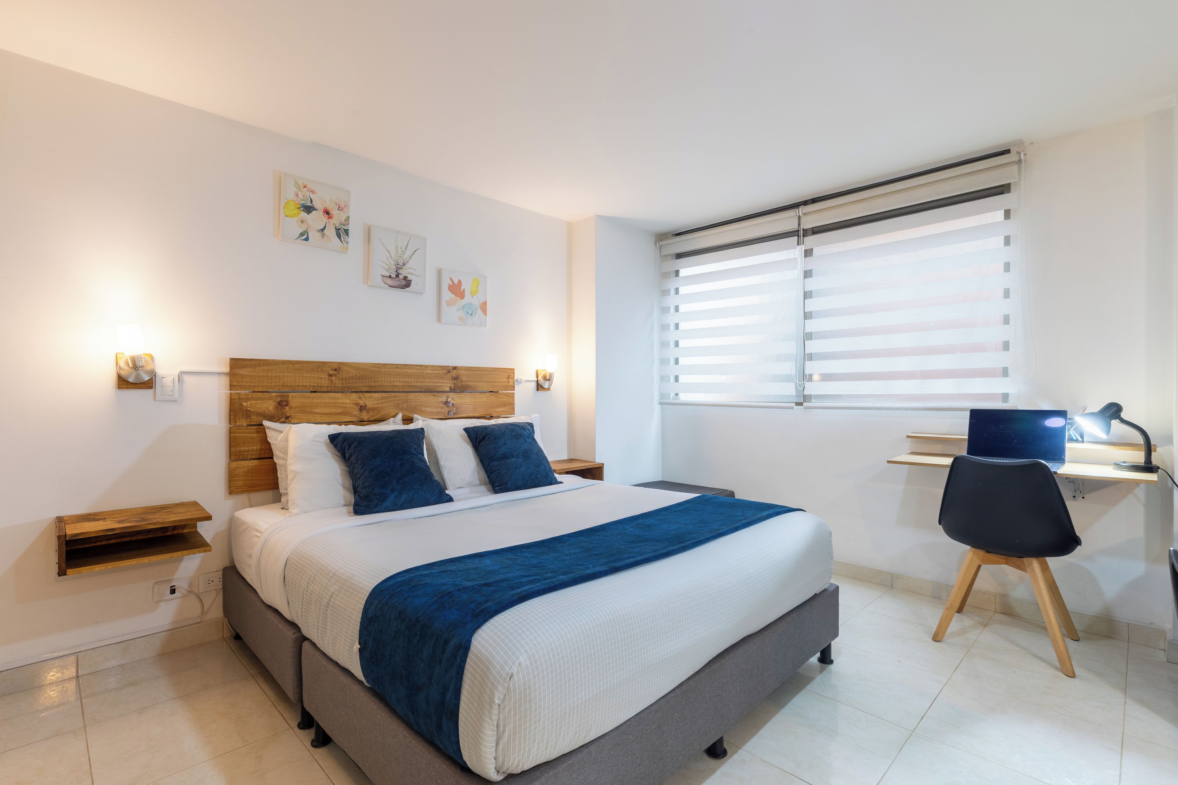 A bedroom with a bed, bedside tables, a desk with a chair, and a window with blinds.