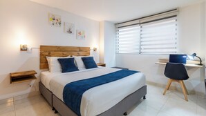 A bedroom with a bed, bedside tables, a desk with a chair, and a window with blinds.